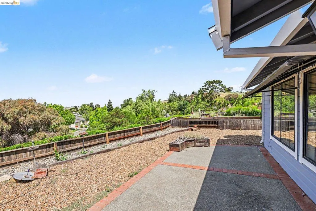 Exterior patio featuring concrete and brick paving, a raised garden bed, and wood fence perimeter