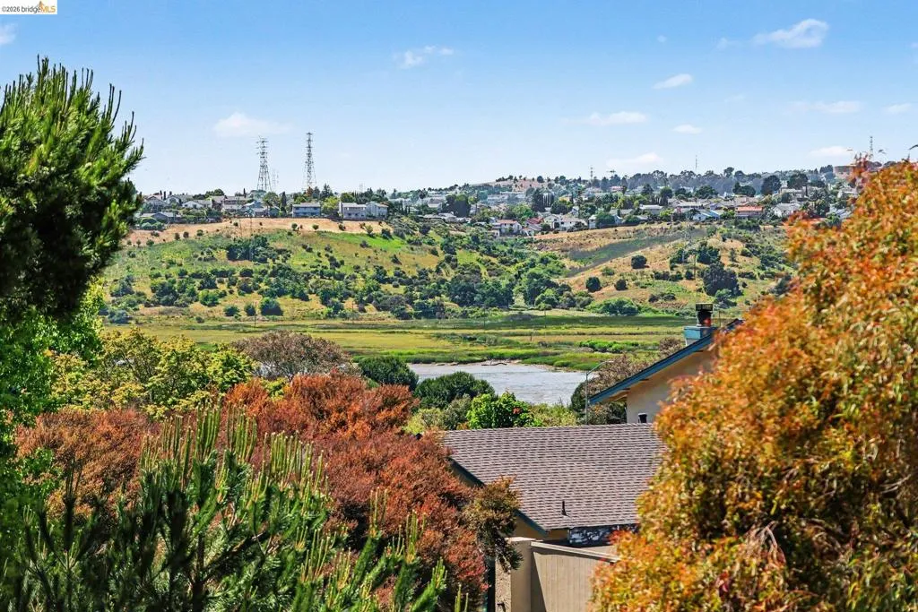 Expansive landscape featuring a distant body of water, rolling hills, and lush natural vegetation