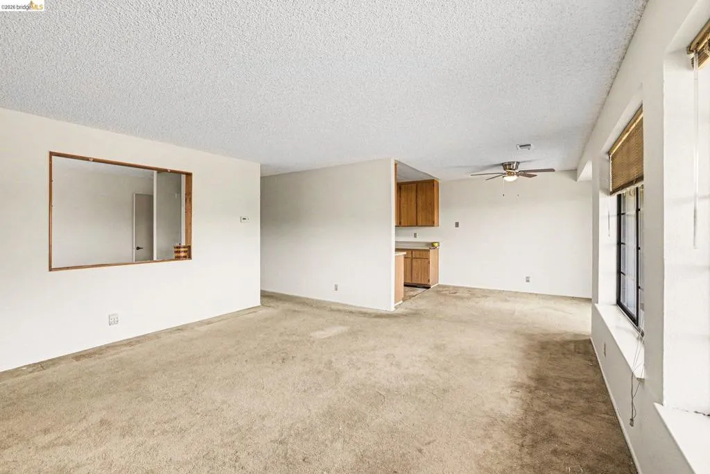 Expansive living area featuring textured ceilings, neutral carpeting, and a pass-through window