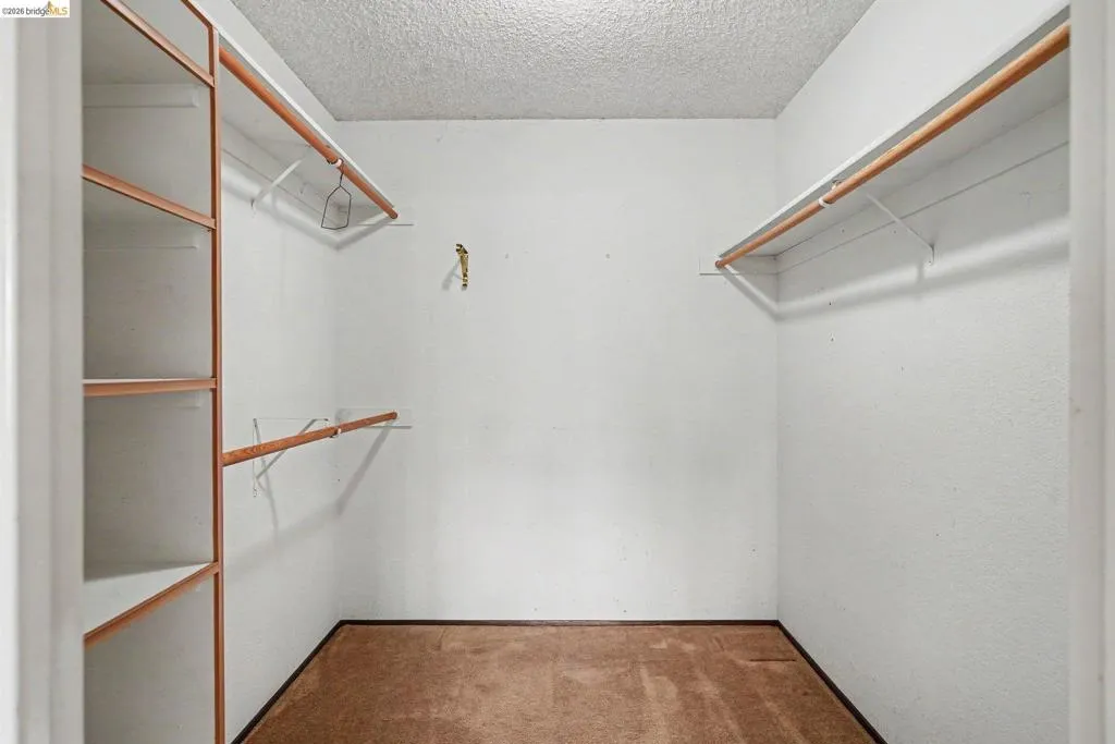 Walk-in closet featuring built-in shelving, dual hanging rods, and textured wall finish