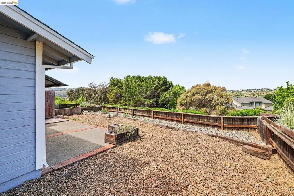 Expansive outdoor space featuring a concrete patio with brick edging, a gravel-covered area, and perimeter fencing
