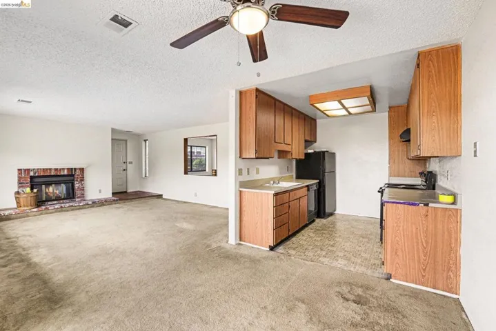 Open-concept living space featuring a brick fireplace, ceiling fan with light fixture, and wood-finish cabinetry in the kitchen area