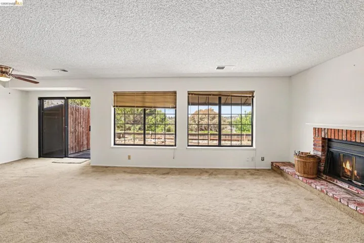 Spacious room featuring neutral carpet flooring, a brick fireplace with a raised hearth, and two large windows