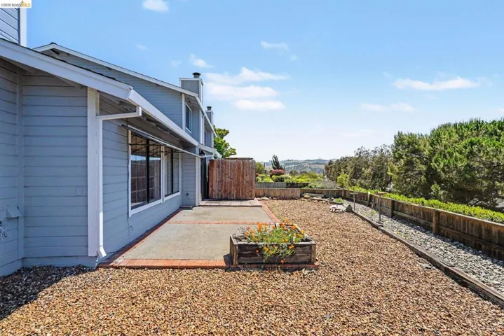 Rear exterior featuring a concrete patio with brick edging, a gravel landscape, a wooden fence, and multiple windows