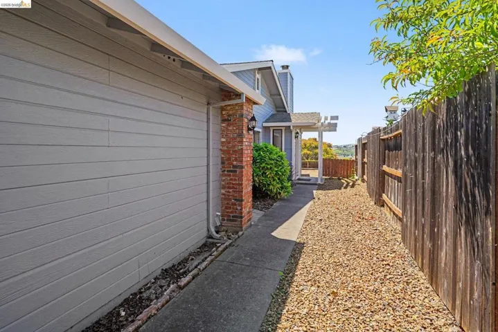 Exterior pathway featuring a concrete walkway, gravel landscaping, and a wood privacy fence