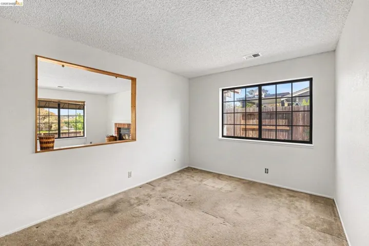 Interior space featuring a pass-through window with wood trim, a multi-pane window with black framing, textured ceiling, white painted walls, and carpet flooring