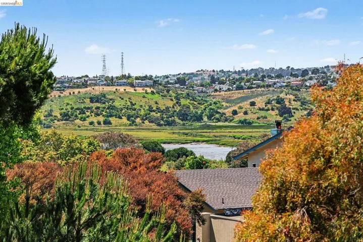 Expansive landscape featuring a distant body of water, rolling hills, and lush natural vegetation
