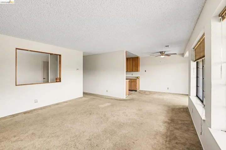 Expansive living area featuring textured ceilings, neutral carpeting, and a pass-through window