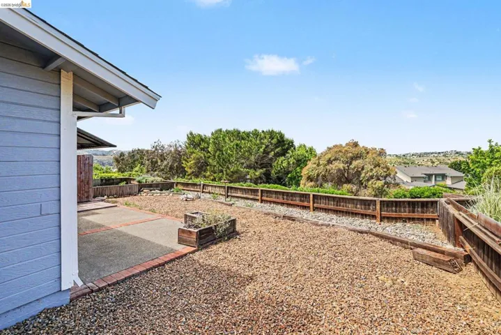 Expansive outdoor space featuring a concrete patio with brick edging, a gravel-covered area, and perimeter fencing