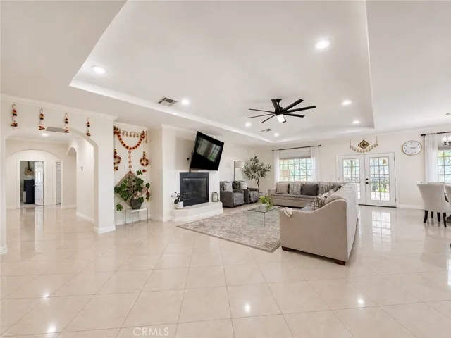 Elegant and expansive family room with fireplace, French doors to backyard shaded patio, and arched door to hallway leading to bedrooms