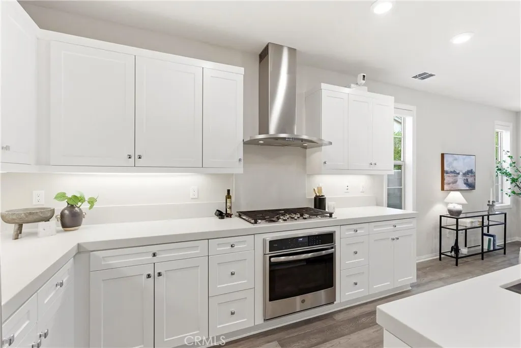 Contemporary kitchen with quartz countertops, stainless steel range hood, gas cooktop, shaker cabinets, and designer finishes throughout.