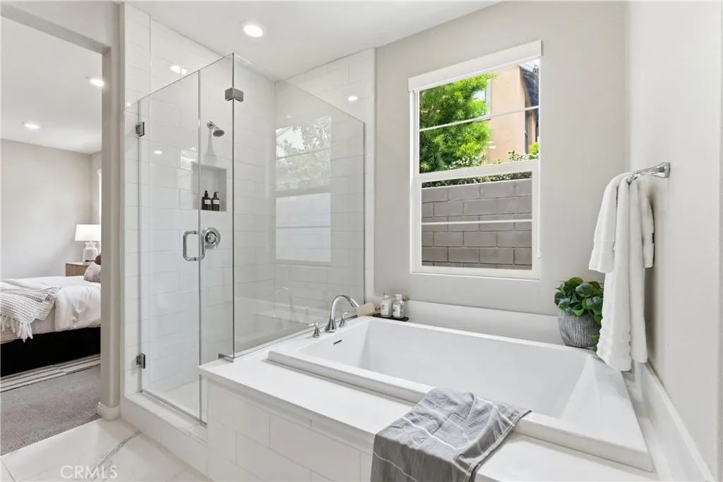 Spa-inspired primary bathroom featuring glass-enclosed walk-in shower, soaking tub, natural light, and modern tile finishes.