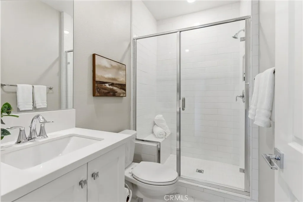 Stylish secondary bathroom featuring quartz vanity, framed mirror, glass-enclosed walk-in shower, and modern white tile finishes.