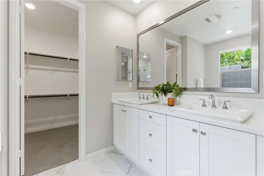 Primary bathroom with dual-sink vanity, quartz countertops, oversized framed mirror, and spacious walk-in closet.