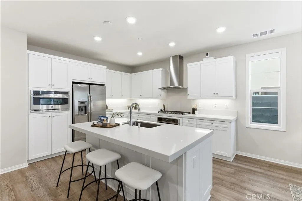 Gourmet kitchen featuring white shaker cabinetry, quartz countertops, stainless steel appliances, oversized center island with seating, and abundant storage.