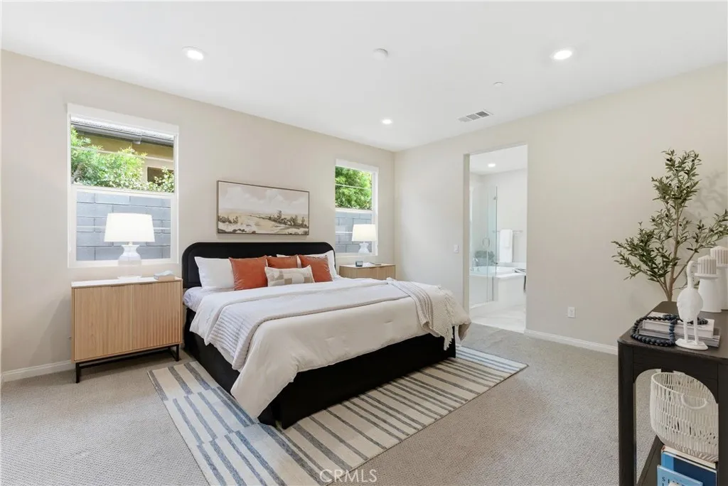 Spacious primary bedroom featuring plush carpeting, large windows for natural light, recessed lighting, and direct access to the en-suite bathroom.