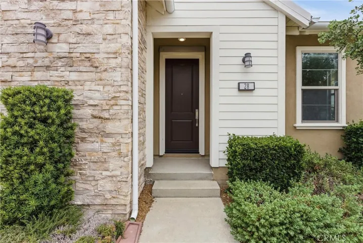 Covered front entry with modern front door, exterior lighting, stone detailing, and landscaped walkway leading into the home.
