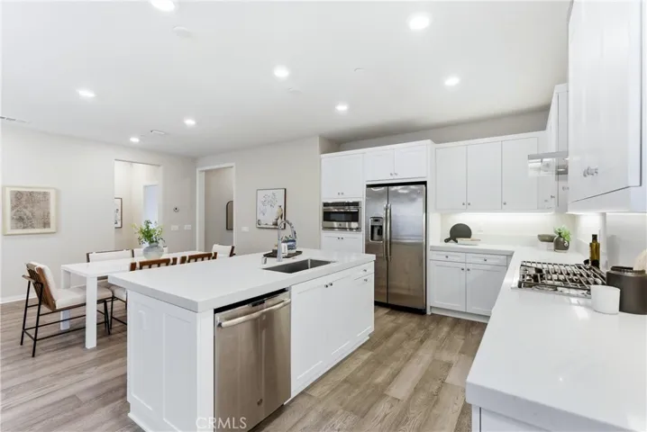 Spacious chef’s kitchen showcasing white cabinetry, stainless steel appliances, recessed lighting, and large center island with integrated dishwasher and seating area.