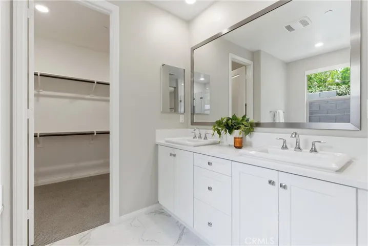 Primary bathroom with dual-sink vanity, quartz countertops, oversized framed mirror, and spacious walk-in closet.