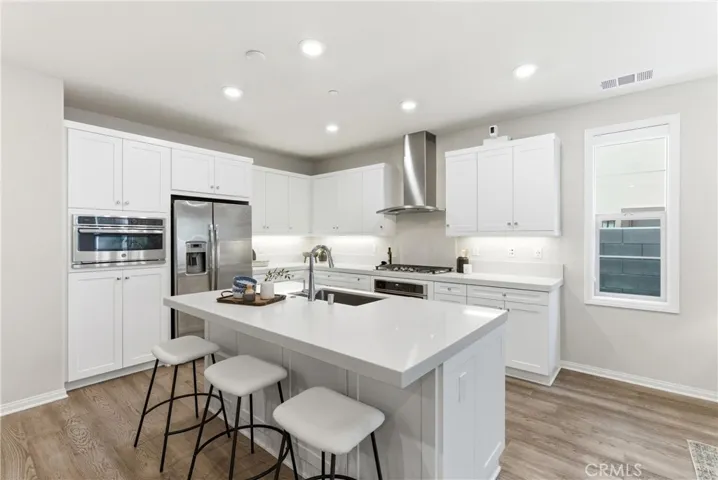 Gourmet kitchen featuring white shaker cabinetry, quartz countertops, stainless steel appliances, oversized center island with seating, and abundant storage.