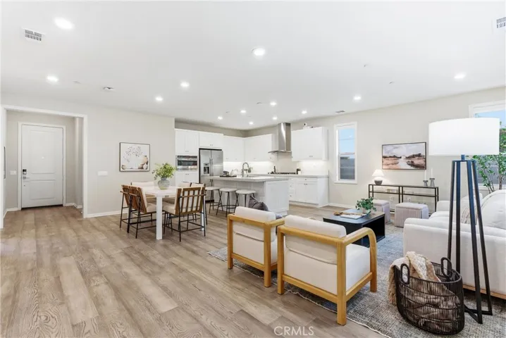 Spacious living room and kitchen area featuring a large center island with seating, stainless steel appliances, white shaker cabinetry, and abundant natural light.