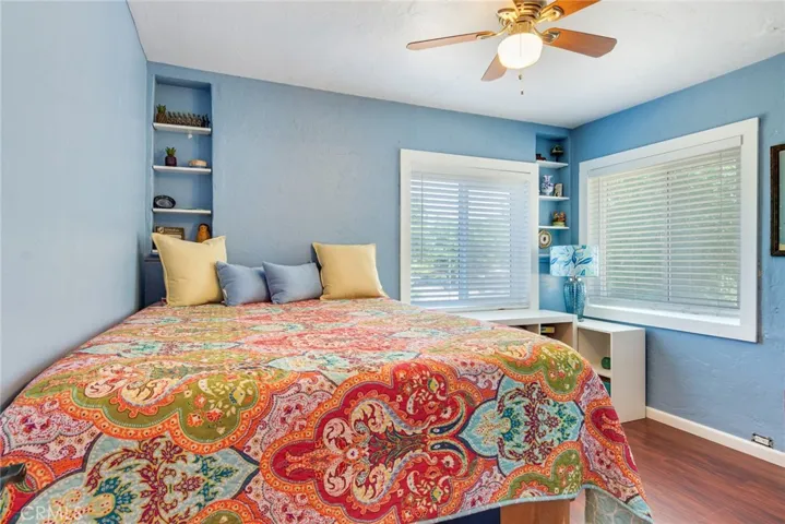 This delightful bedroom has framed widows, a ceiling fan with light, and built in shelving.