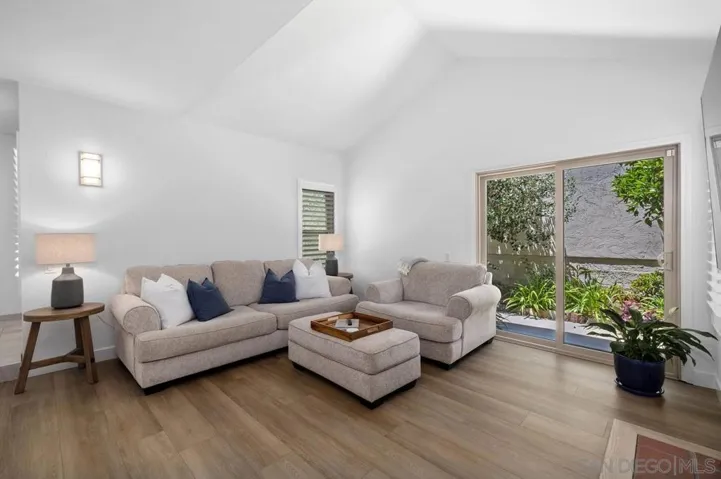 Spacious living room with vaulted ceiling, plantations shutters, sliding door to a beautifully landscaped side yard, fireplace, luxury vinyl flooring.