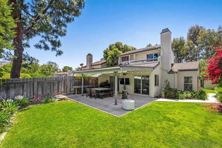 Expansive backyard with covered patio, large grassy areas, and lush plantings. 40+ shrubs and trees were planted and irrigation system updated in 2024.
