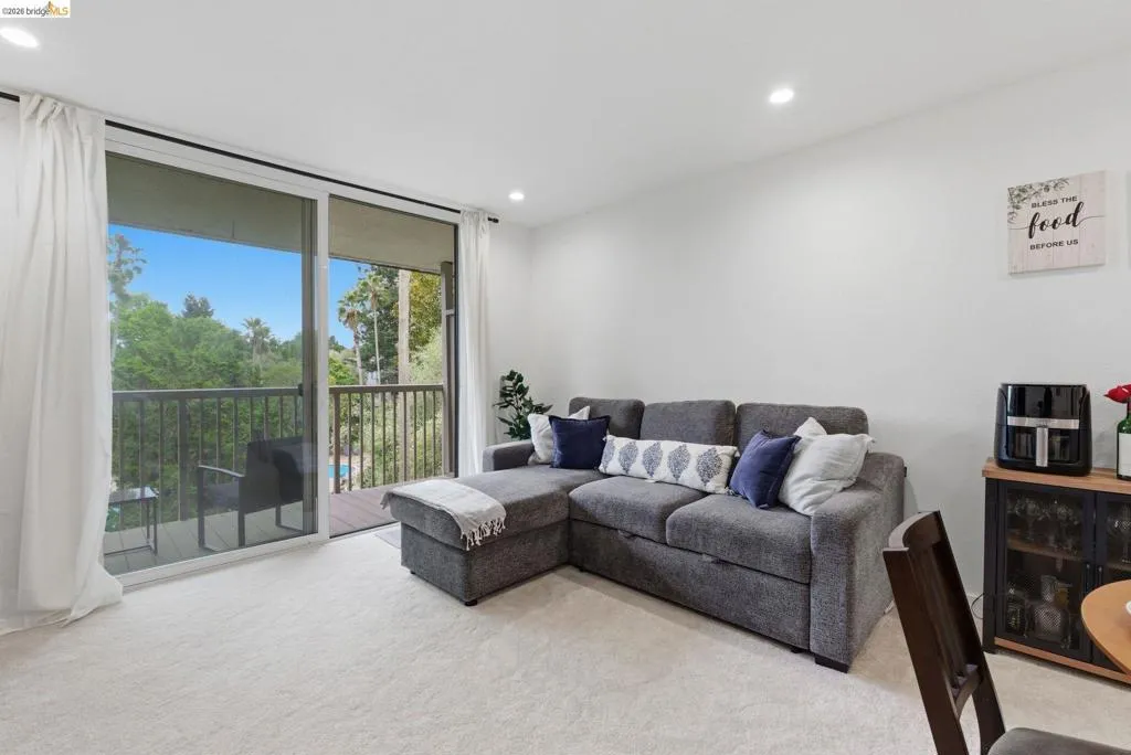 Living area featuring light-toned carpeting and a full-height sliding glass door leading to an exterior balcony