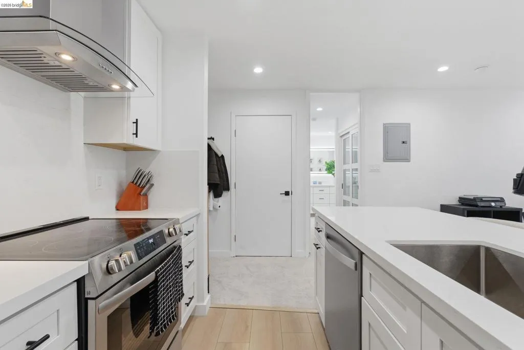 Modern kitchen featuring white cabinetry, stainless steel appliances, light-toned countertops, and light wood-finish flooring