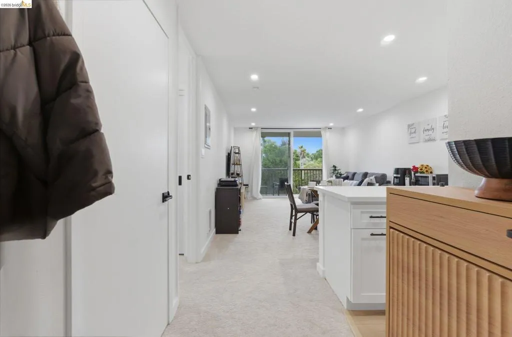 Open-concept living area featuring a kitchen island with white cabinetry and dark hardware, recessed lighting, and a private balcony