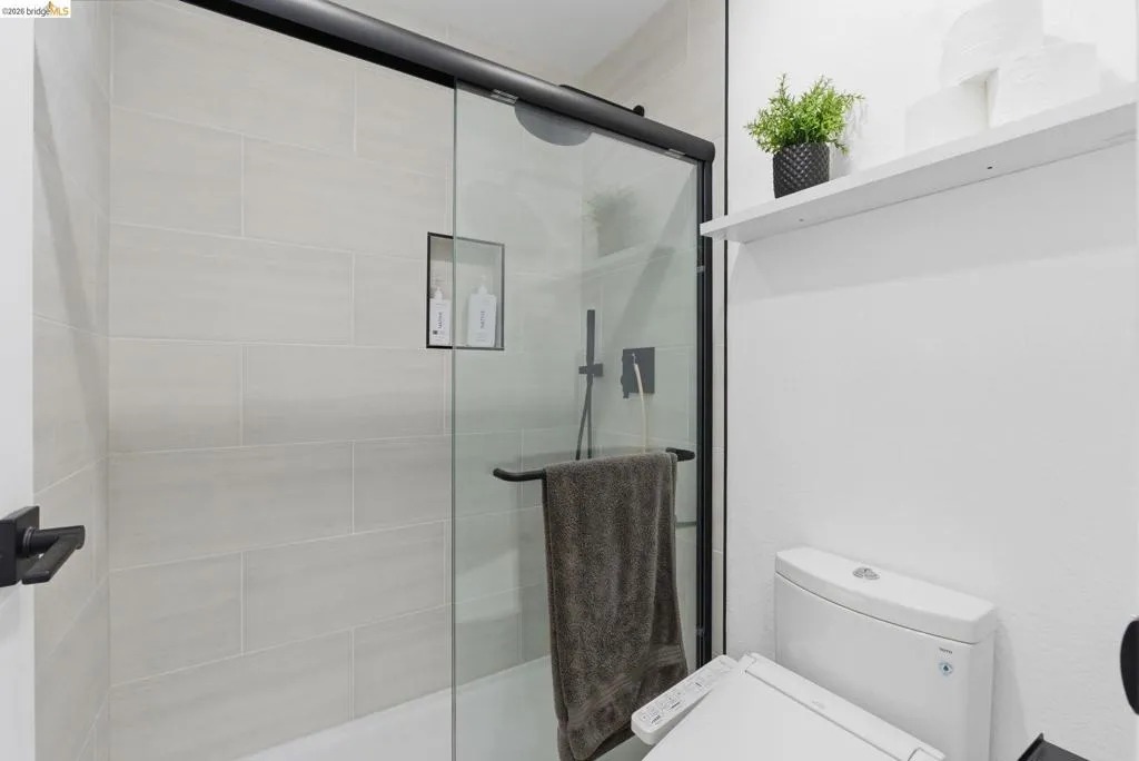 Modern bathroom featuring a glass-enclosed shower with matte black hardware, light-toned horizontal tile, a built-in shower niche, and a white toilet