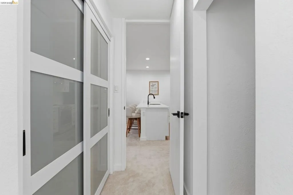 Hallway with white walls, carpet flooring, modern sliding doors with frosted glass panels, and black hardware