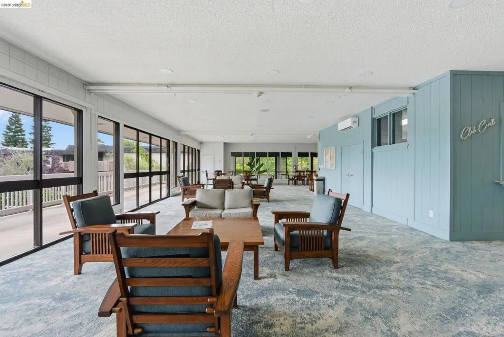 Spacious common area featuring extensive window walls, recessed lighting, light blue accent wall paneling, and patterned carpet flooring
