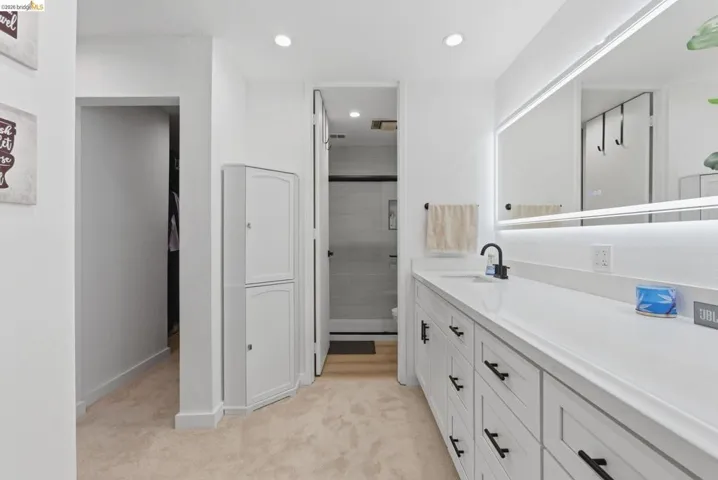 Contemporary bathroom featuring a white vanity with ample storage, a single black faucet, a large back-lit mirror, recessed ceiling lights, and a white storage cabinet