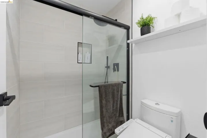 Modern bathroom featuring a glass-enclosed shower with matte black hardware, light-toned horizontal tile, a built-in shower niche, and a white toilet