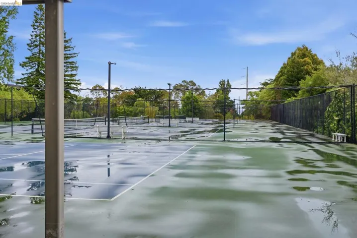 Spacious outdoor tennis court complex featuring multiple courts, perimeter fencing, and surrounding mature landscaping