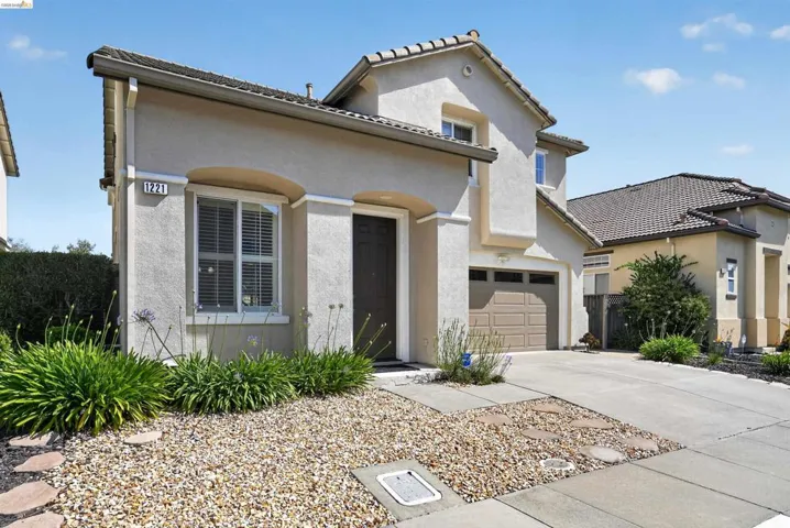 Stucco exterior with arched architectural details, a tiled roof, an integrated garage, a concrete driveway, and front landscaping featuring gravel and plantings