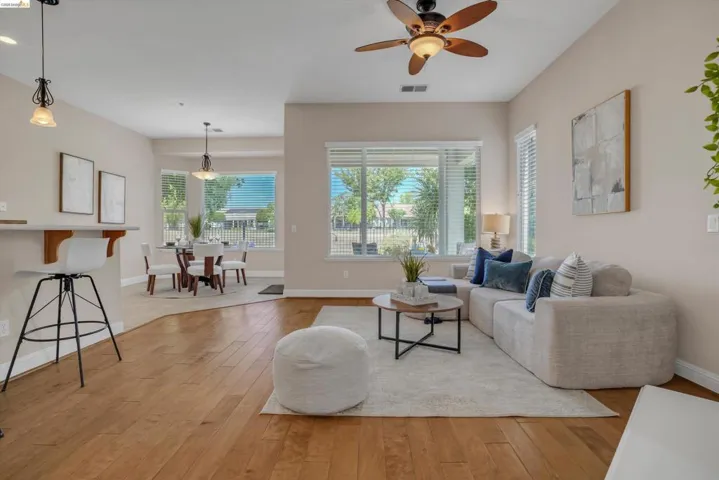 Open-concept living space featuring wood-finish flooring, a ceiling fan with integrated lighting, and multiple windows with blinds