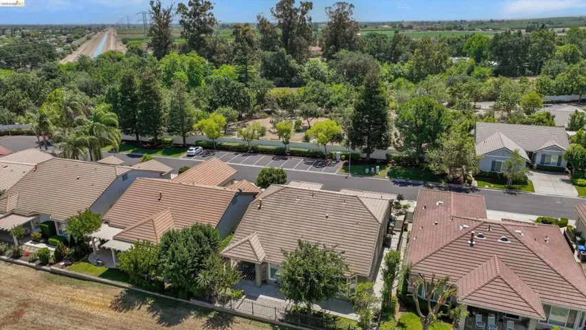 Aerial perspective showcasing properties with tile roofs and manicured landscaping, bordering a tree-lined greenbelt and canal