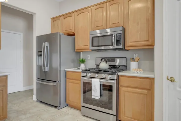 Kitchen featuring wood cabinetry, light-toned countertops, stainless steel appliances, and tiled flooring