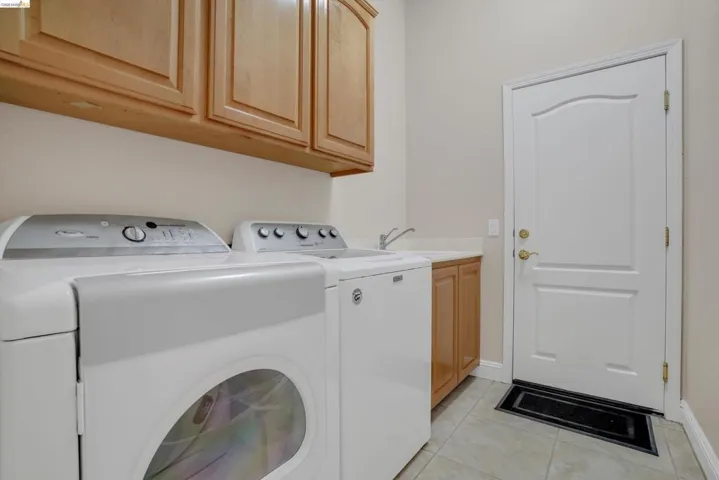 Laundry room featuring light wood-finish cabinetry, a utility sink with a chrome faucet, and tiled flooring