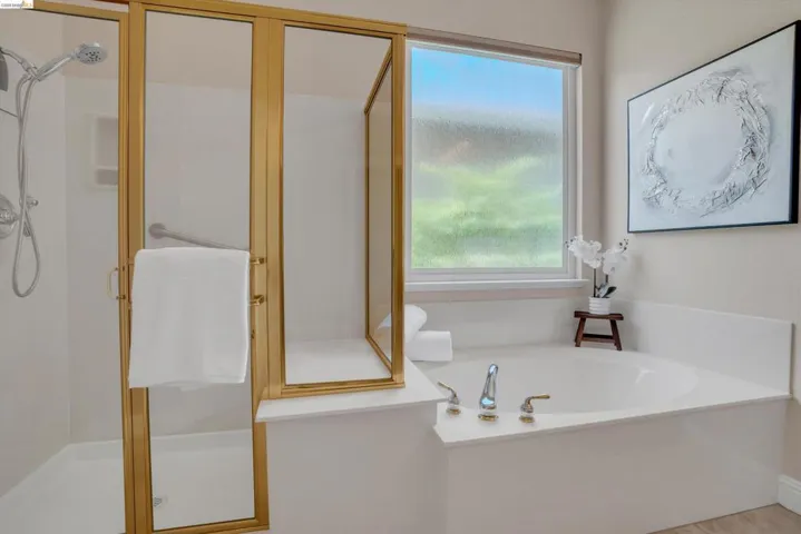 Bathroom featuring a built-in tub with deck-mounted fixtures, a separate shower with a gold-finish frame, and a frosted window