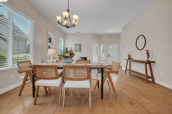 Dining area featuring wood-finish flooring, a decorative chandelier, and a large window with blinds