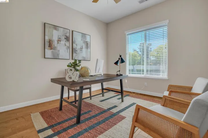 Light-filled room featuring wood-finish flooring, a ceiling fan, and a large window with blinds