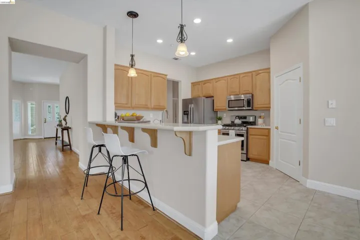 Kitchen featuring light wood-finish cabinetry, stainless steel appliances, and a breakfast bar with pendant lighting
