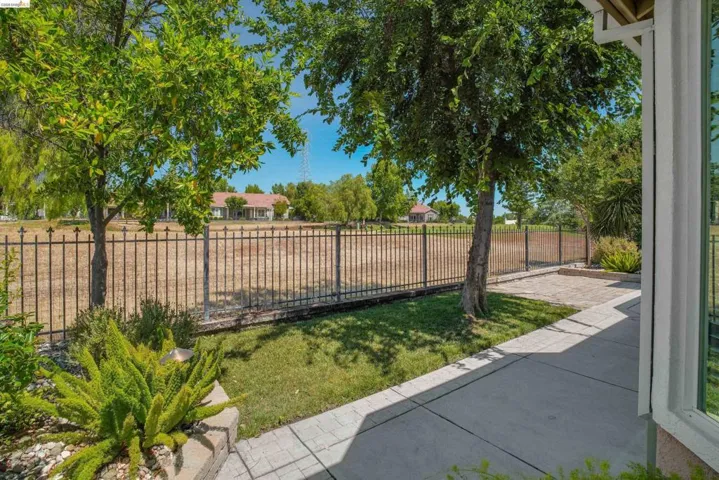 Patio area featuring a concrete pathway and paver section, bordered by a wrought iron fence and mature trees