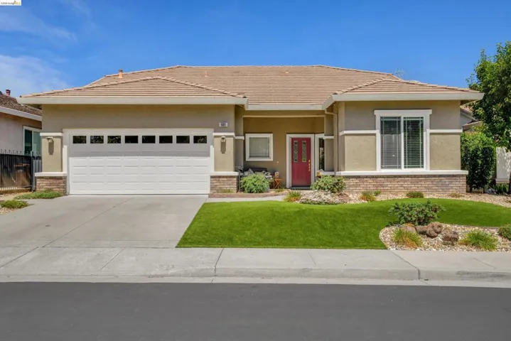 Single-story stucco exterior featuring a red entry door, an attached two-car garage with transom windows, a tile roof, and stone-finish accents