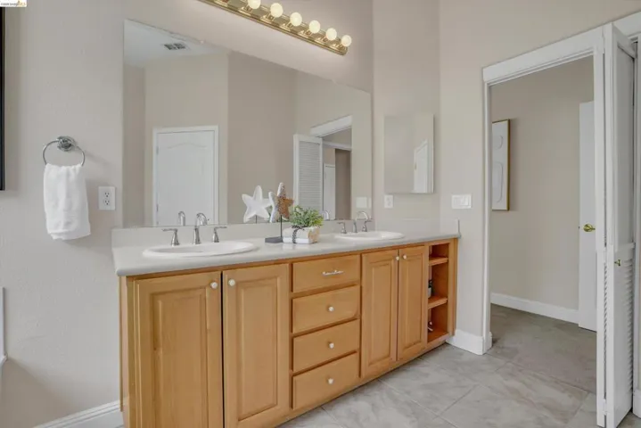 Dual vanity with light wood cabinetry and integrated sinks, complemented by a large mirror and overhead multi-bulb lighting fixture