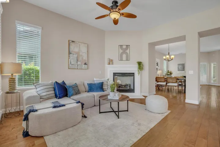 Inviting living area featuring a fireplace with a white mantel, wood-finish flooring, and a ceiling fan